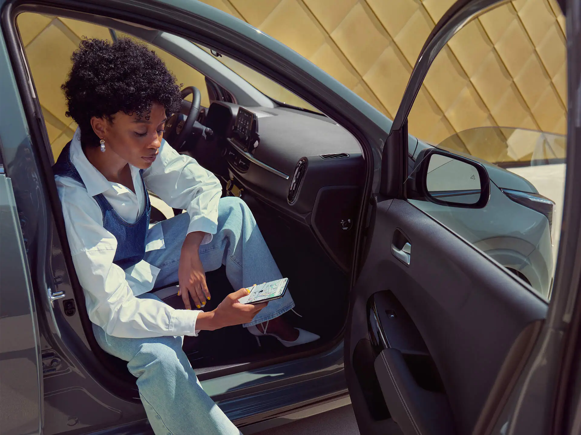Eine Person sitzt im geöffneten Auto und schaut auf ein Smartphone.