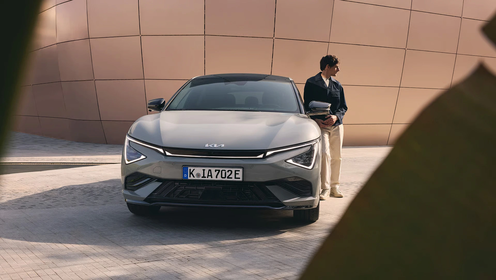Ein Kia EV6 steht vor einer modernen Wand, daneben eine Person.