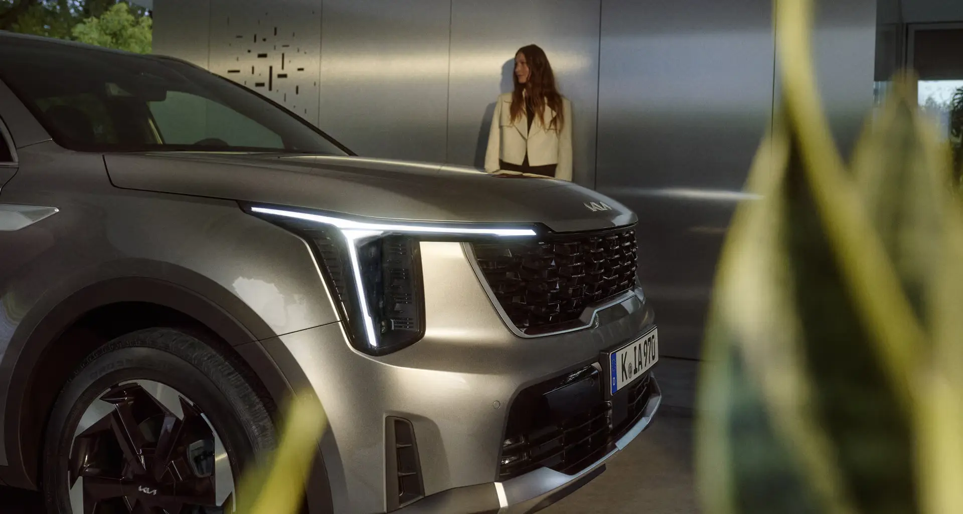 Ein silberner Kia Sorento steht in einer modernen Umgebung, eine Frau im Hintergrund.