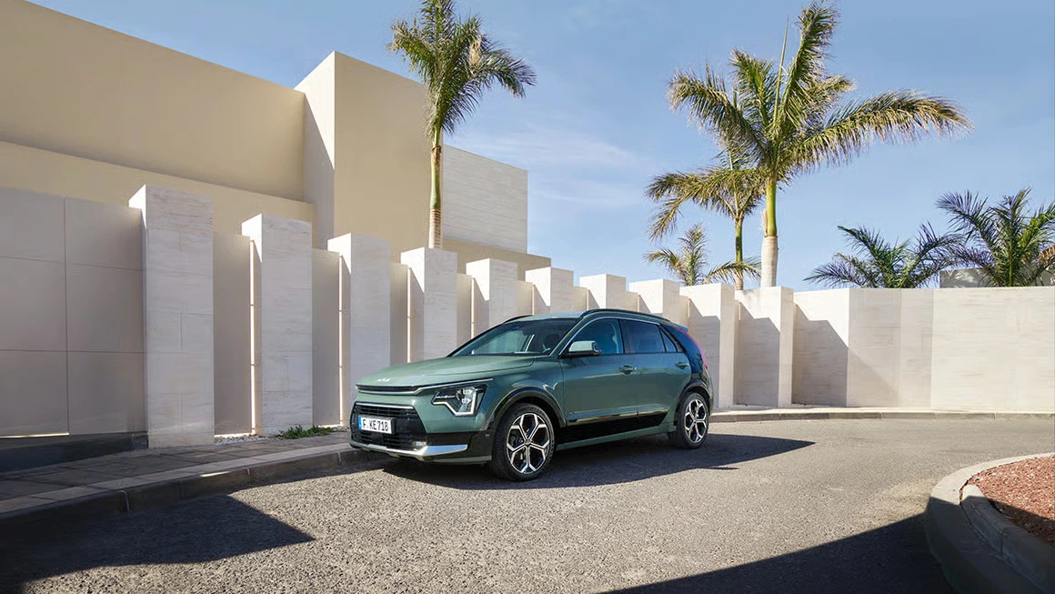 KIA Niro Auto steht vor einer modernen, weißen Wand mit Palmen im Hintergrund.