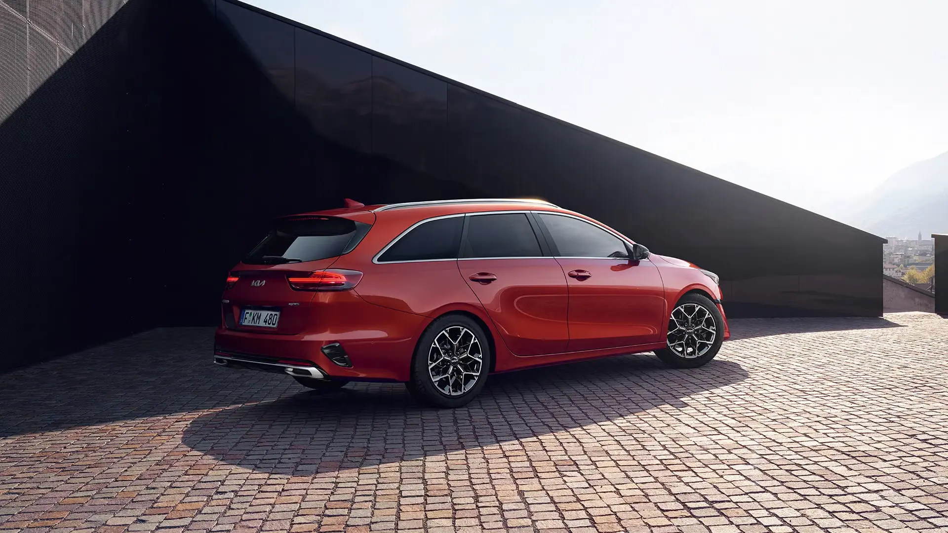 Roter Kia Ceed SW steht auf gepflastertem Platz vor modernem Gebäude.