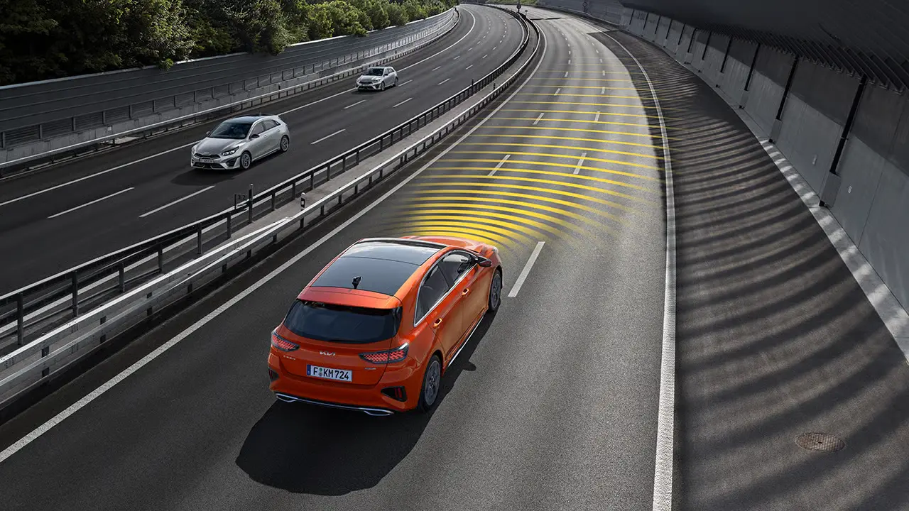 Ein orangefarbener Kia Ceed fährt auf einer Autobahn mit sichtbaren Sensorstrahlen.