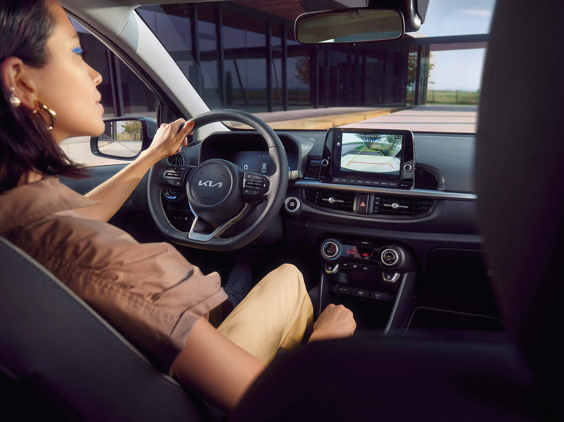 Eine Person sitzt am Steuer eines Kia Picanto und schaut auf den Bildschirm mit Rückfahrkamera.