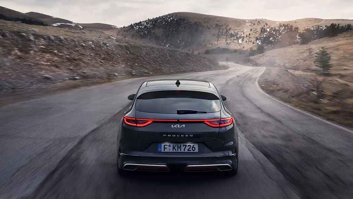 2-Slider-kia-proceed Ein schwarzer Kia Proceed fährt auf einer kurvigen Landstraße in hügeliger Landschaft.
