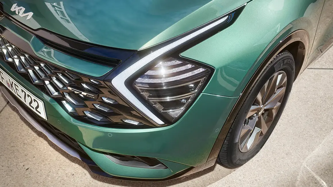Nahaufnahme der Front eines grünen Kia Sportage mit markantem Kühlergrill und Scheinwerfer.