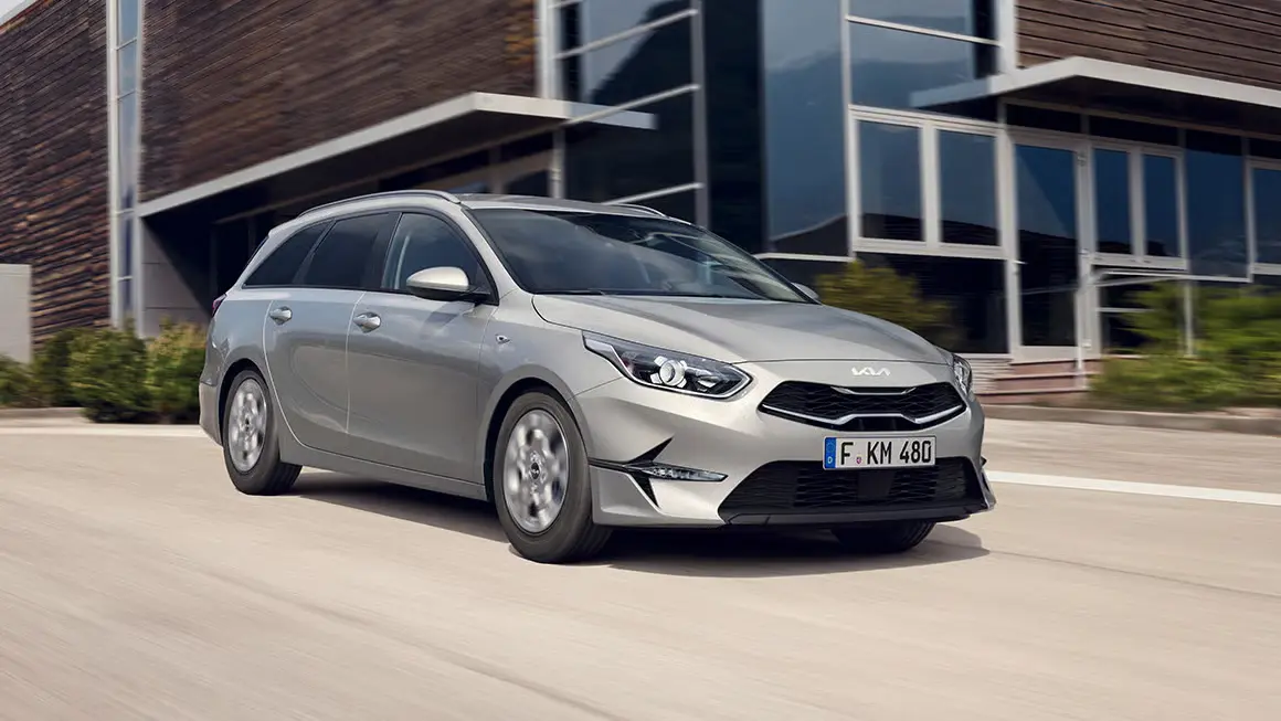 Silberner Kia Ceed Sportswagon fährt auf einer Straße vor einem modernen Gebäude.