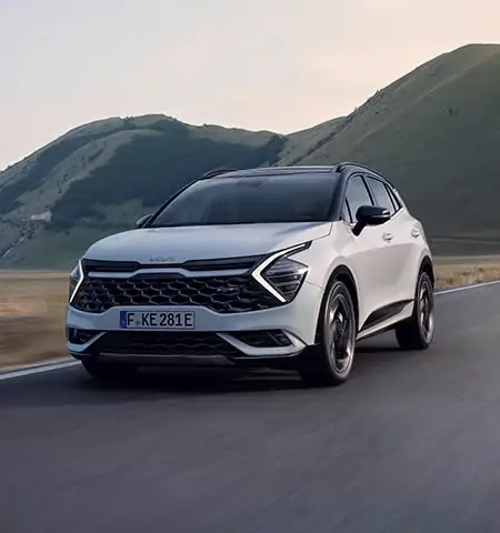 Ein weißer Kia Sportage fährt auf einer Landstraße vor einer hügeligen Landschaft.