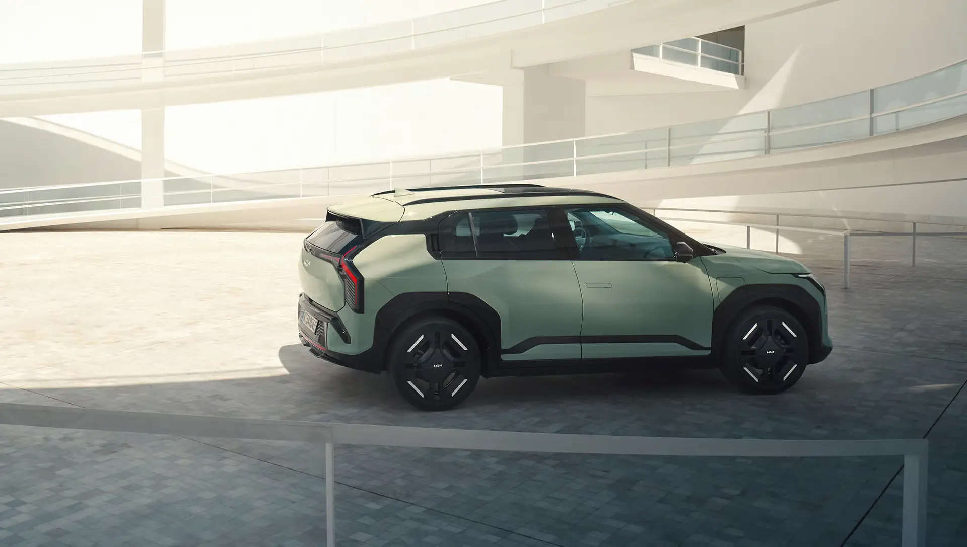 Ein grüner Kia EV3 steht in einem modernen, hellen Innenhof.