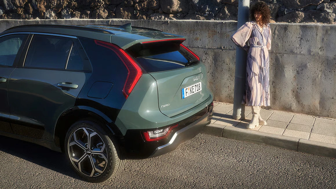 KIA Niro in einer städtischen Umgebung, neben einer Person an einer Steinmauer.