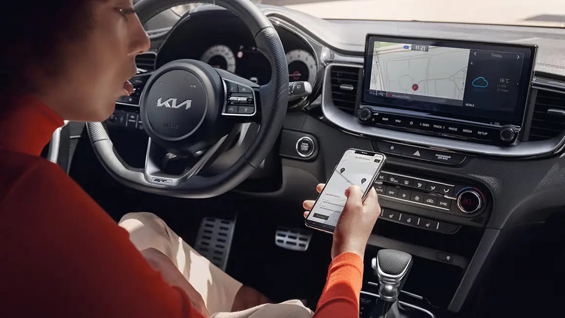 Person im Inneren eines Kia-Fahrzeugs bedient ein Smartphone vor dem Armaturenbrett.