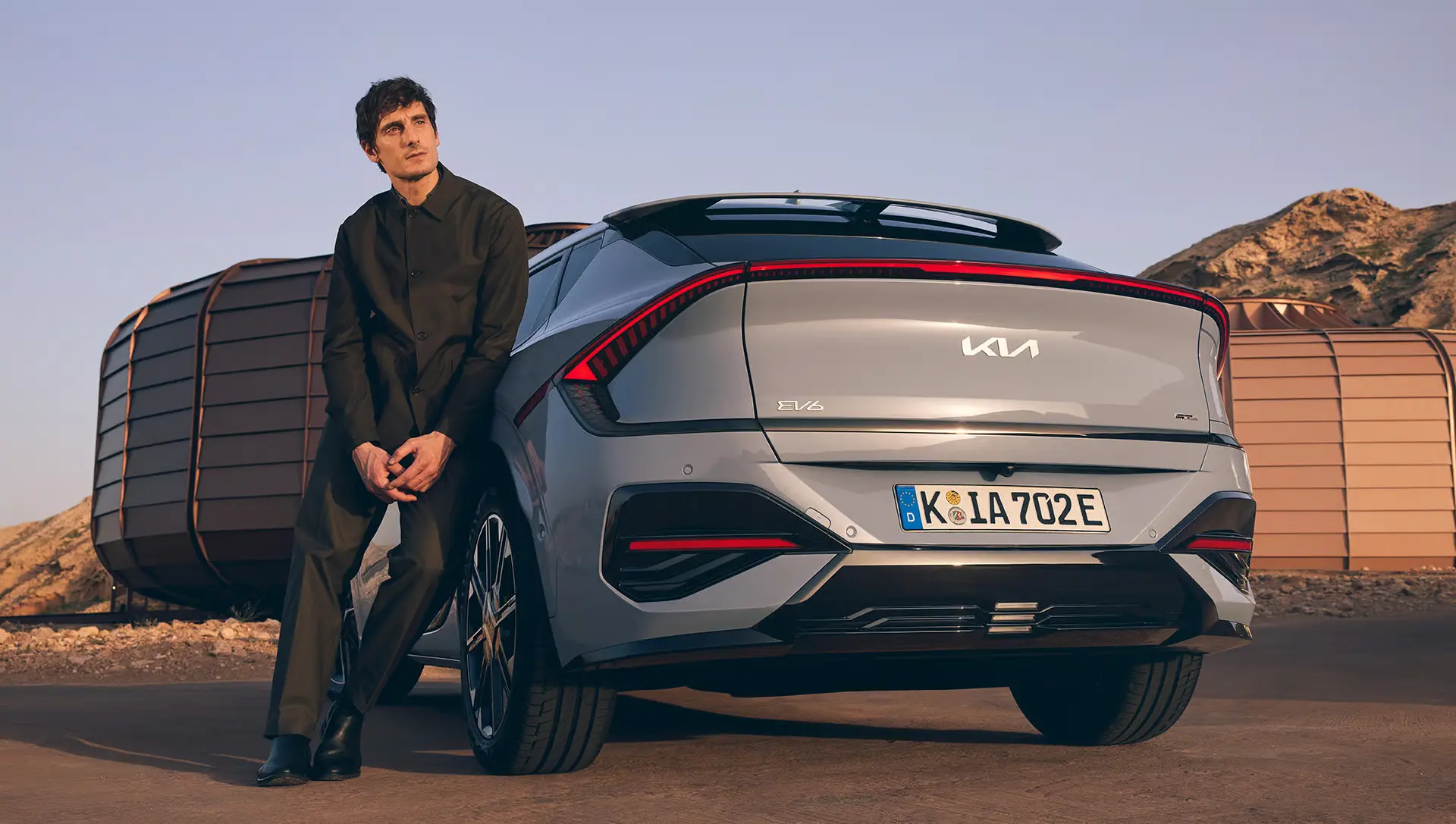 Ein Mann lehnt an einem grauen Kia EV6 mit modernem Design.