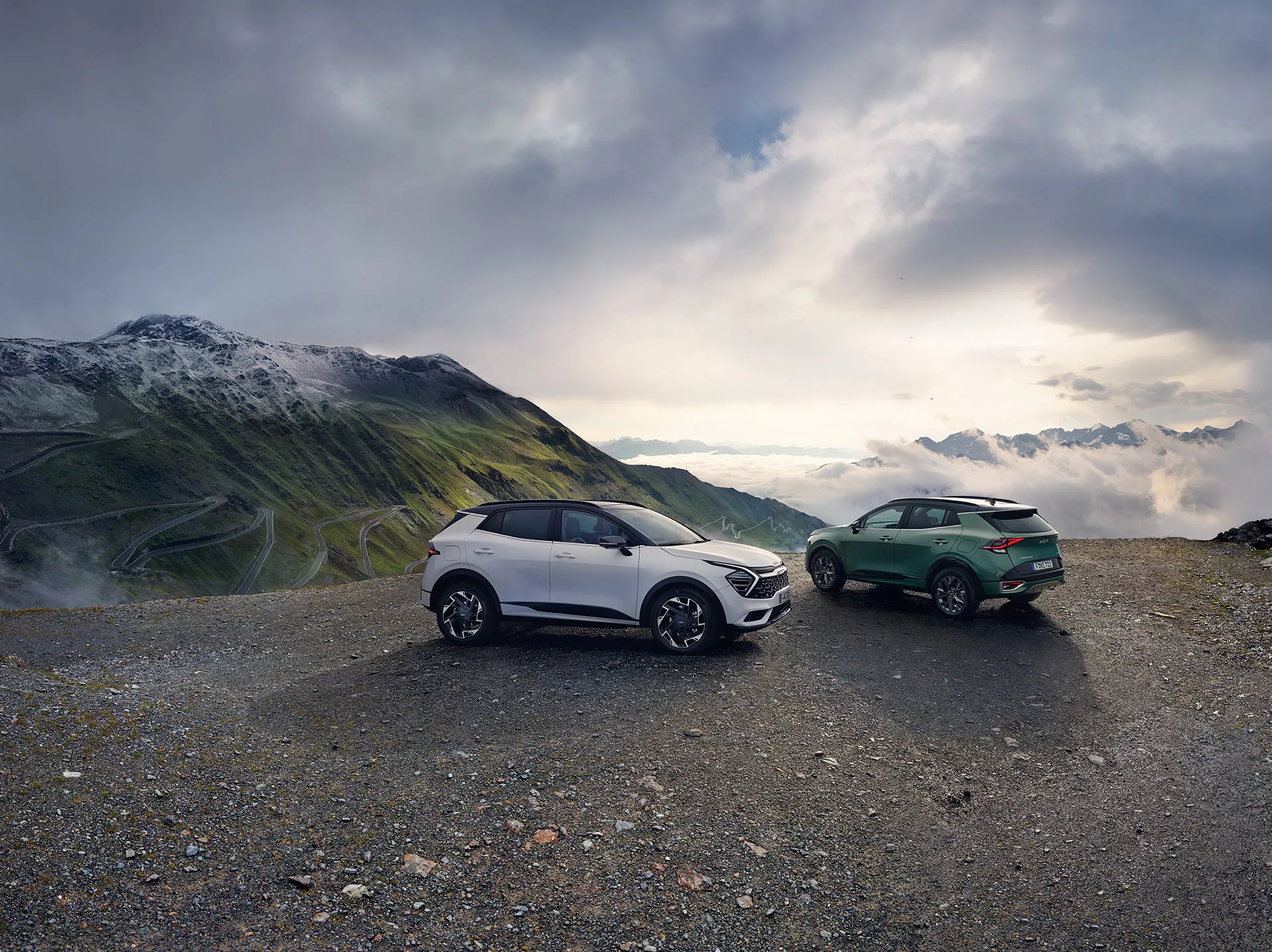 Zwei Kia Sportage SUVs stehen auf einem Bergplateau mit einer malerischen Berglandschaft im Hintergrund.