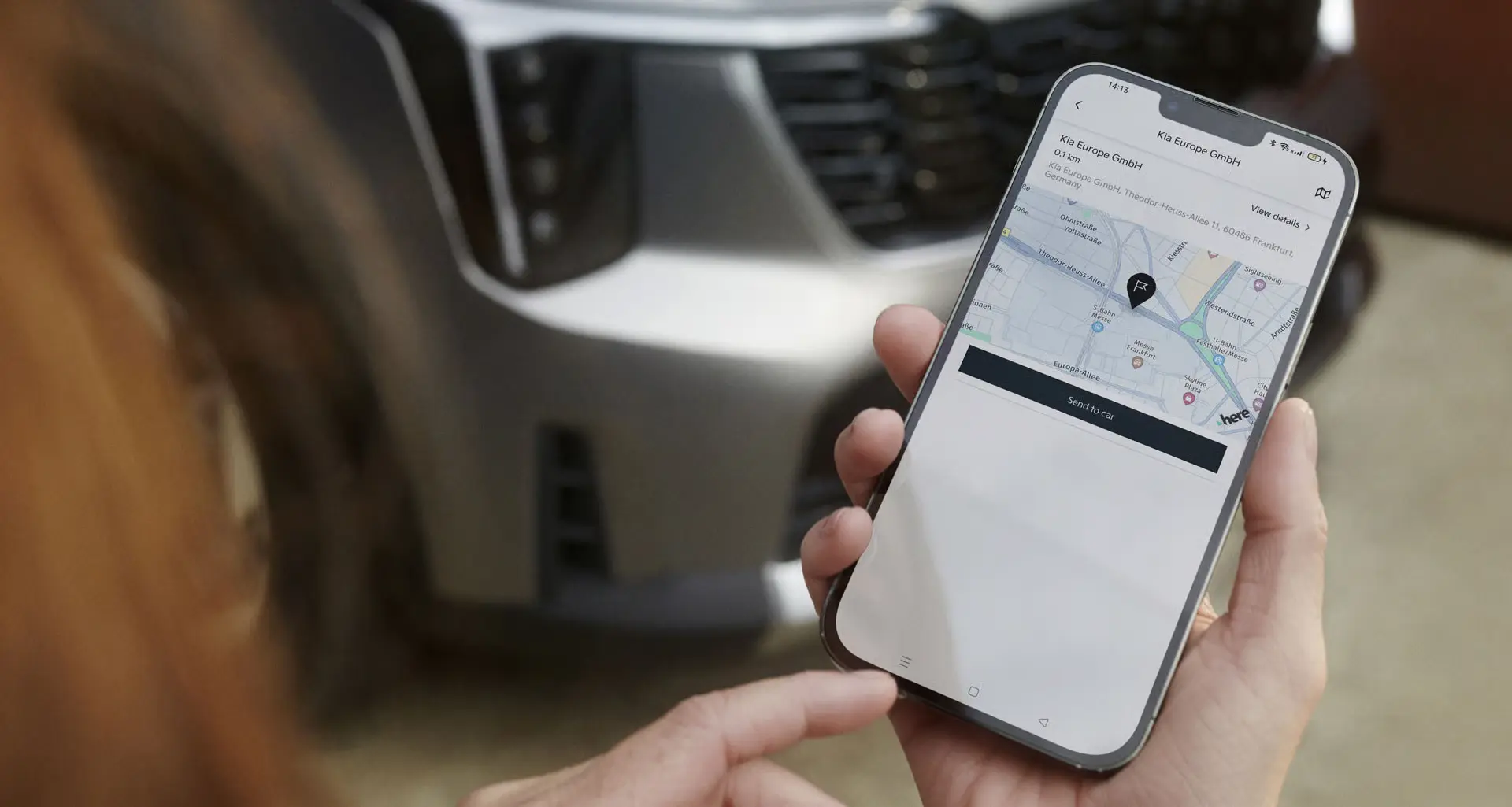 Person hält ein Smartphone mit einer Navigations-App vor einem Kia-Fahrzeug.