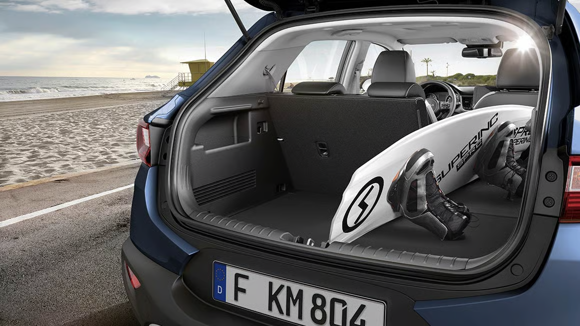 Kofferraum eines Kia Stonic mit einem Surfbrett am Strand.