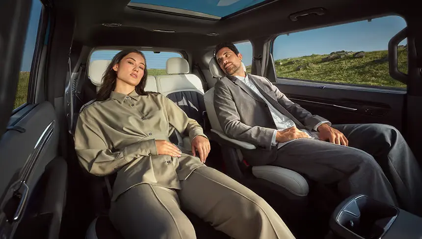 Zwei Personen entspannen in den Rücksitzen eines Autos mit Panorama-Glasdach.