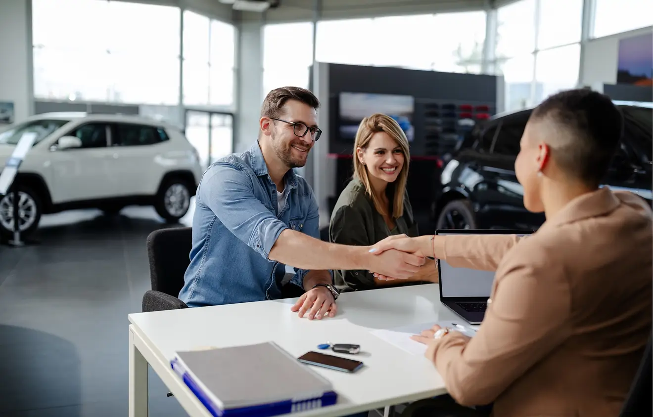 Fahrzeug in guten Händen 2 Personen schütteln sich in einem Autohaus die Hände, während sie einen Autokauf abschließen.