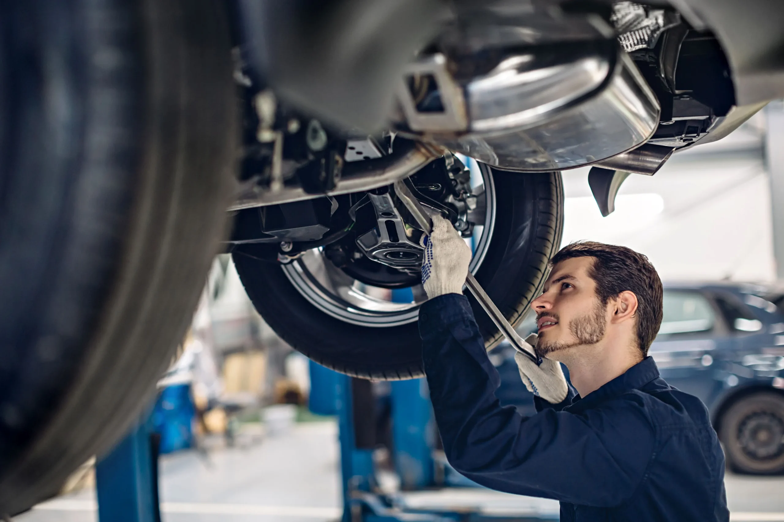 Kia-Werkstatt Mechaniker arbeitet unter einem Auto an einem Reifen in einer Werkstatt.