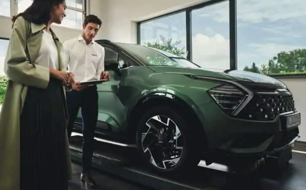 Eine Frau und ein Mann stehen neben einem grünen Kia-SUV in einem Autohaus.