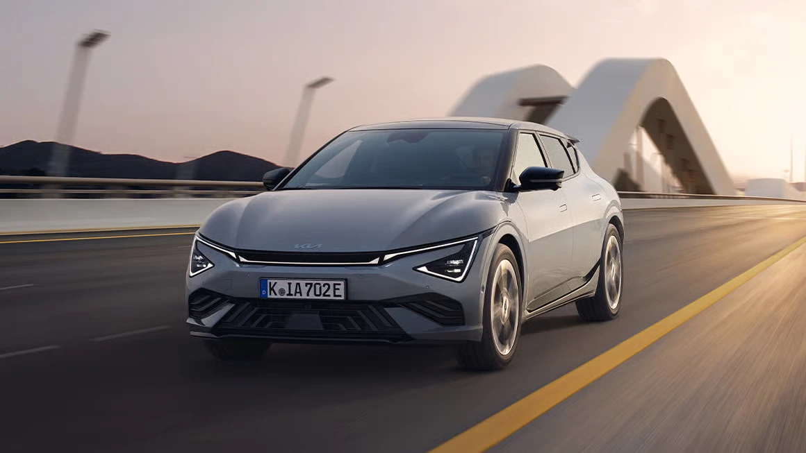 Kia EV6 GT fährt über eine moderne Brücke bei Sonnenuntergang.