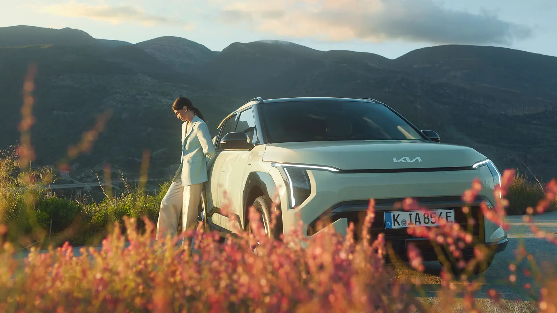Eine Person steht neben einem weißen Kia EV3 vor einer Berglandschaft.