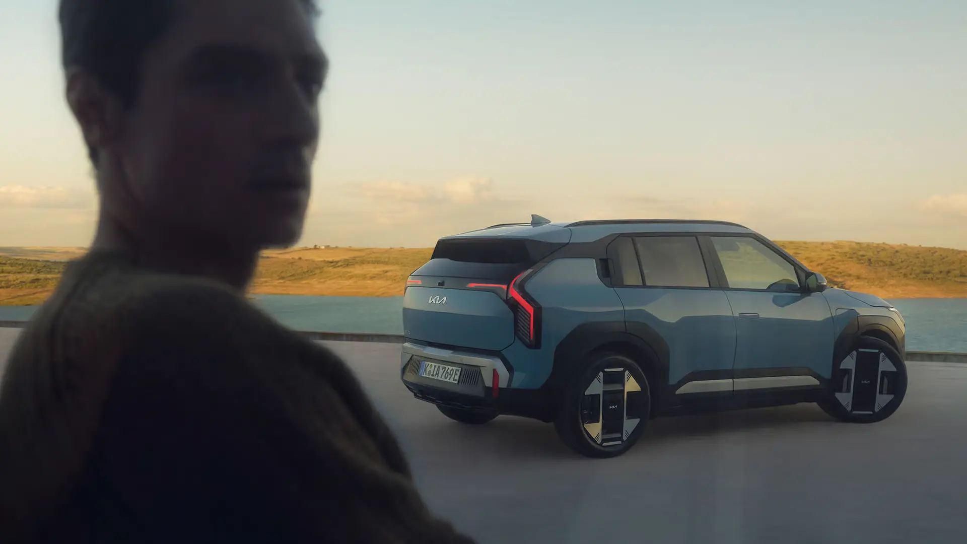 Ein blauer Kia EV3 steht vor einer Landschaft mit Wasser und Hügeln im Hintergrund.