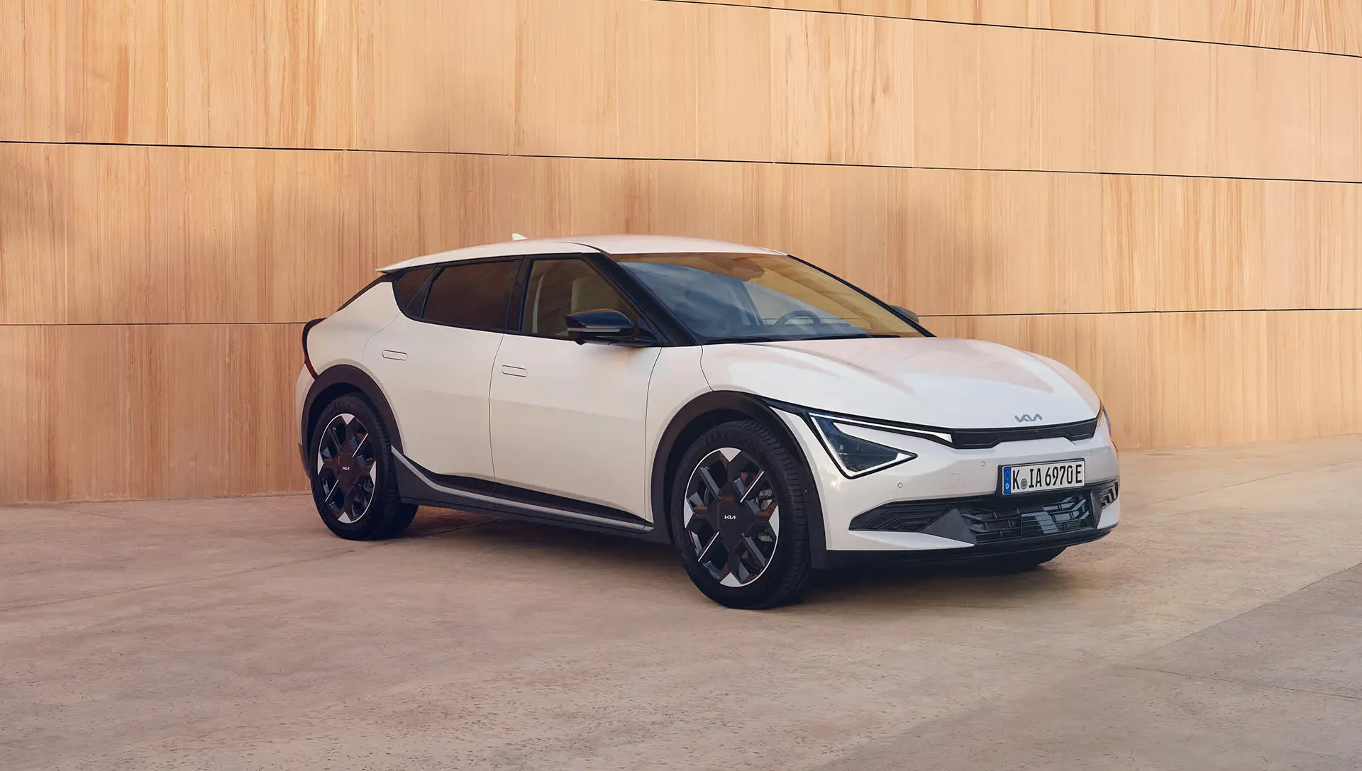 Ein weißer Kia EV6 steht vor einer Holzfassade.