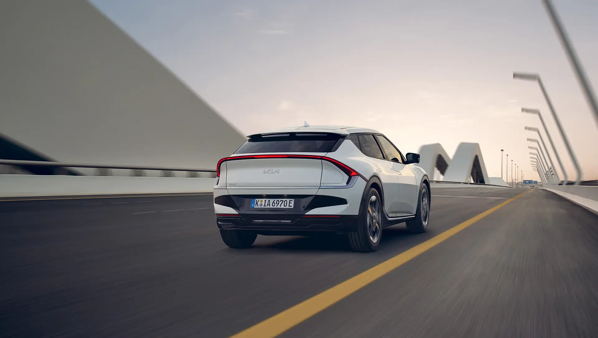 Ein weißer Kia EV6 fährt auf einer modernen Brücke.