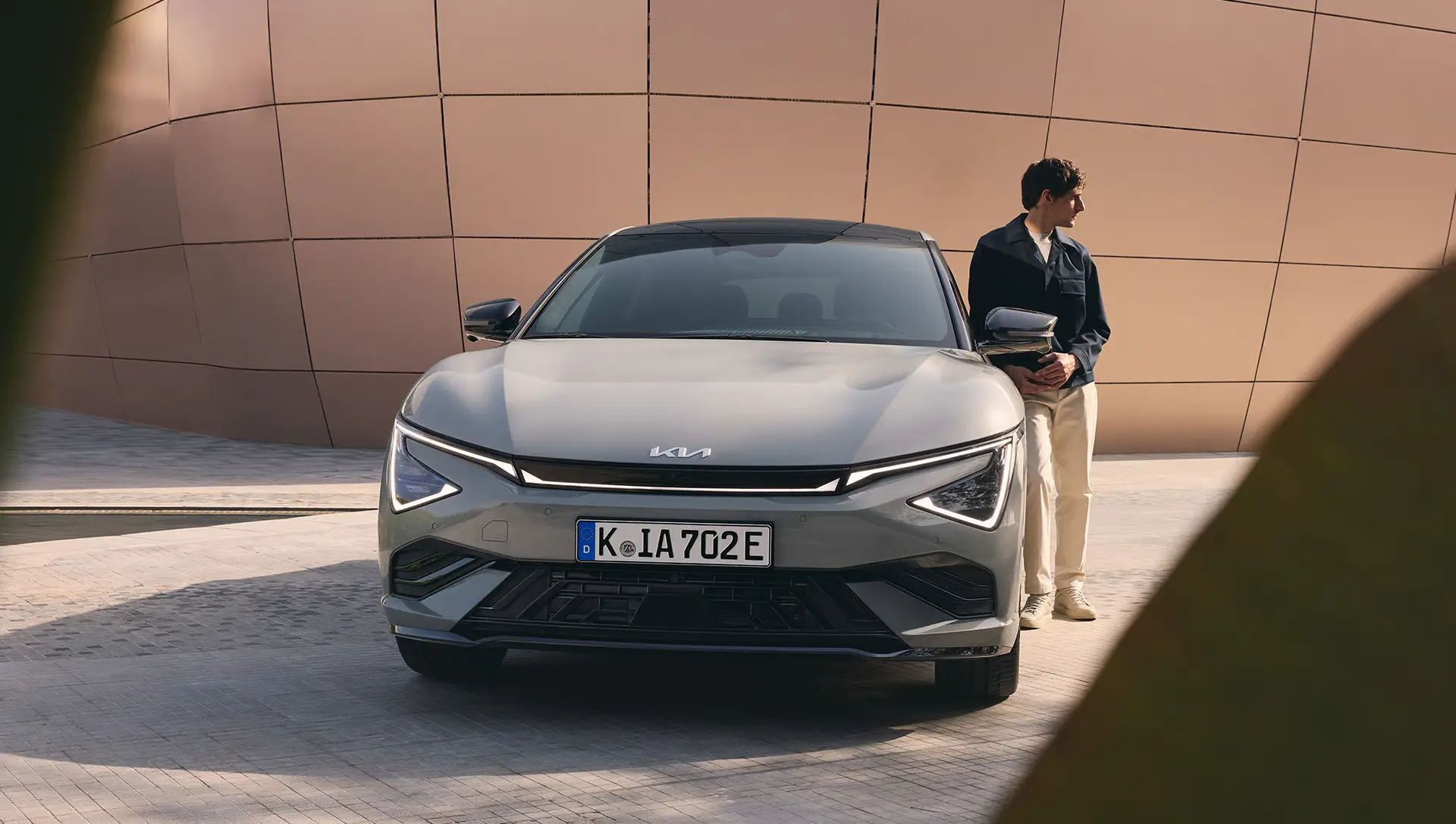 Ein Kia EV6 steht vor einem modernen Gebäude, daneben eine Person.