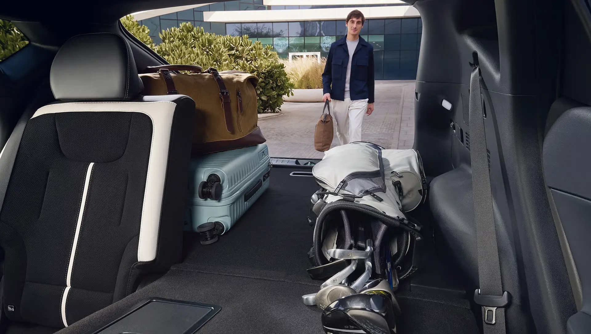 Kofferraum eines Kia EV6 mit Gepäck und Golfset, während eine Person auf das Auto zugeht.