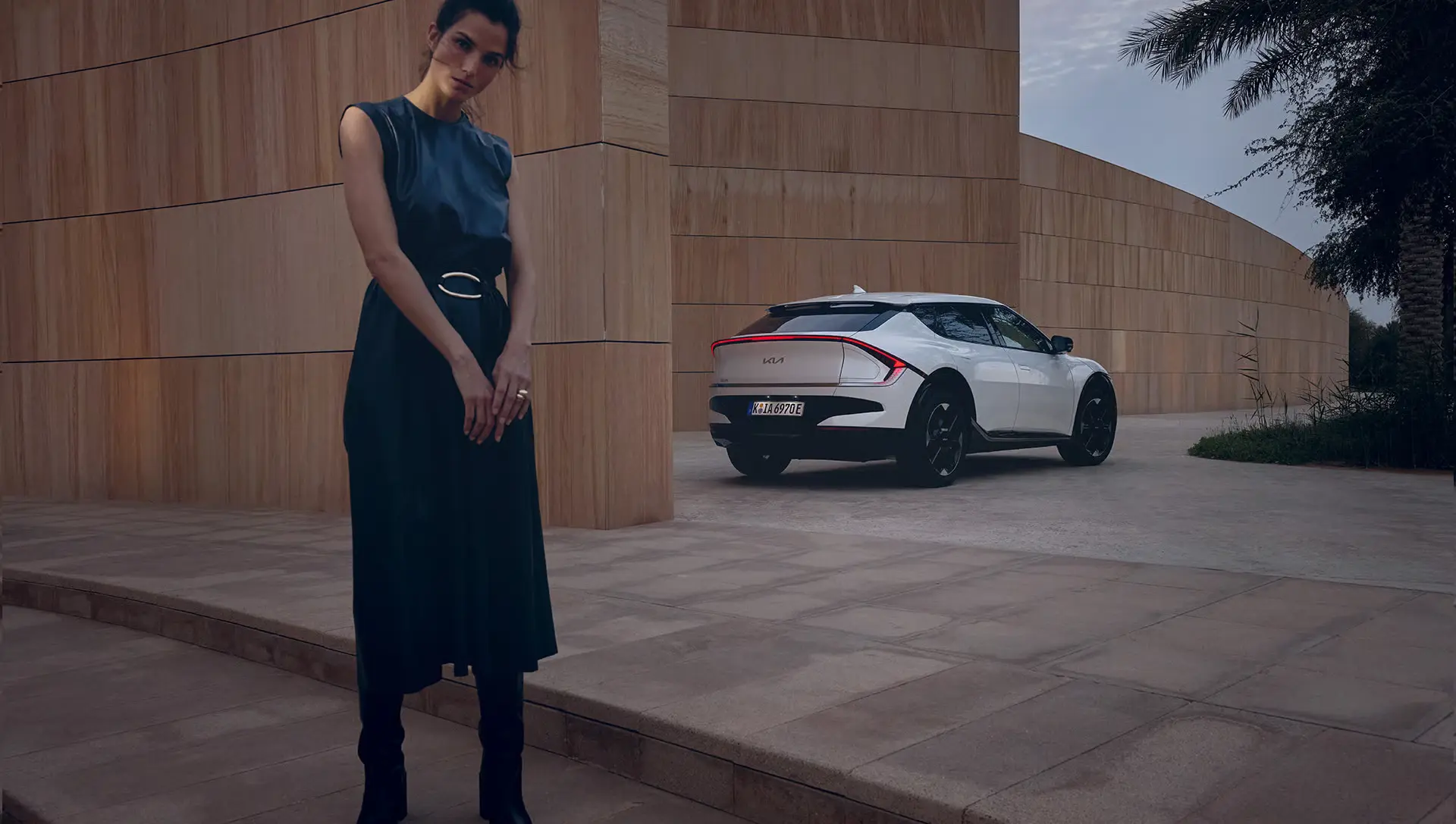Eine Frau steht vor einem weißen Kia EV6 auf einem modernen Platz.