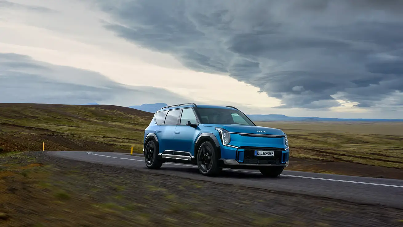 Blauer Kia EV9 SUV auf einer Küstenstraße bei Sonnenuntergang.