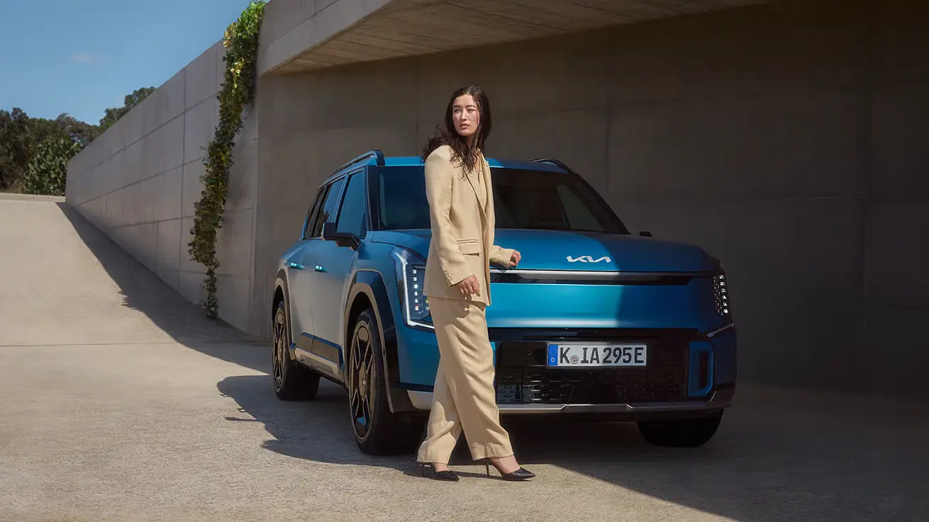 Eine Frau steht neben einem blauen Kia EV9.