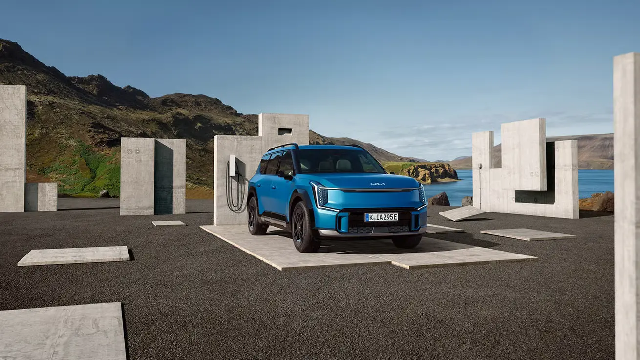 Ein blauer Kia EV9 steht an einer Ladestation in einer landschaftlichen Umgebung.