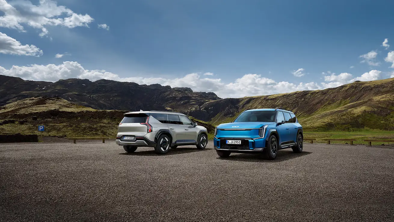 Zwei Kia EV9 Autos stehen auf einem Parkplatz vor einer bergigen Landschaft.