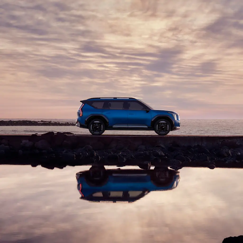 Ein blauer Kia EV9 SUV steht vor einem Meereshorizont bei Sonnenuntergang.