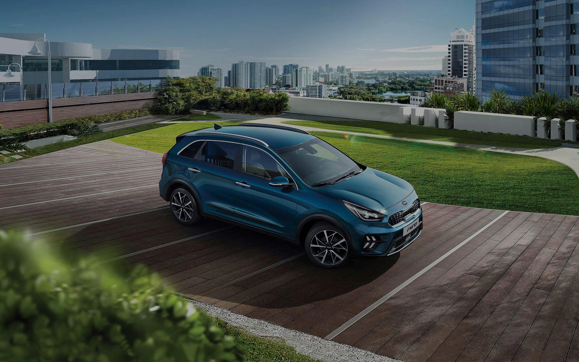 Ein blauer Kia Niro steht auf einem Parkplatz mit Stadtblick im Hintergrund.