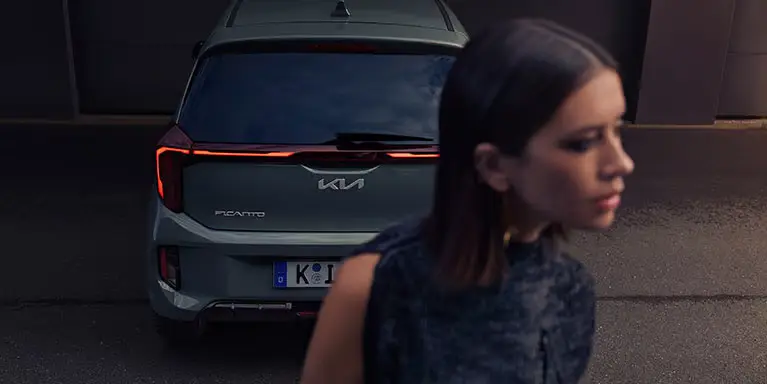 Ein Kia Picanto GTL steht auf einer Straße, im Vordergrund eine unscharfe Frau.