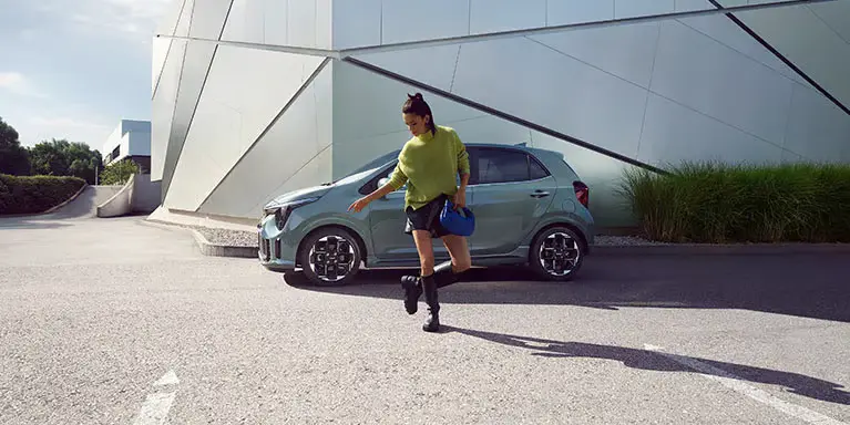 Eine Frau geht vor einem geparkten Kia Picanto GTL MY25.
