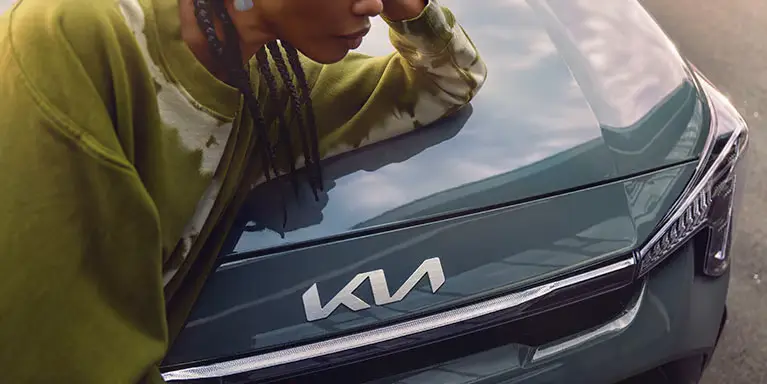 Person lehnt sich auf die Motorhaube eines Kia Picanto mit sichtbarem Logo.