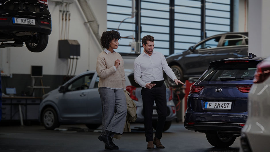 Eine Frau und ein Mann stehen in einer Autowerkstatt neben einem blauen Kia.