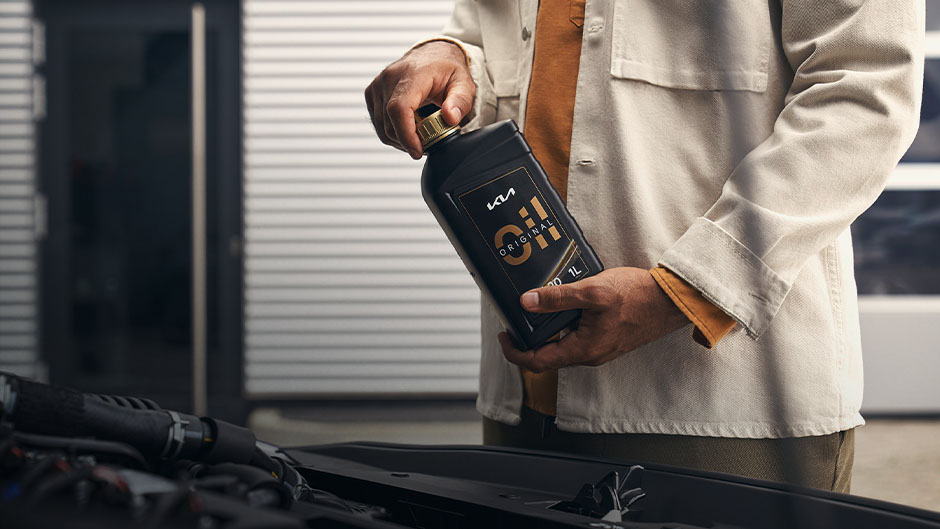 Eine Person hält eine Flasche KIA-Motoröl über einem offenen Motorraum.