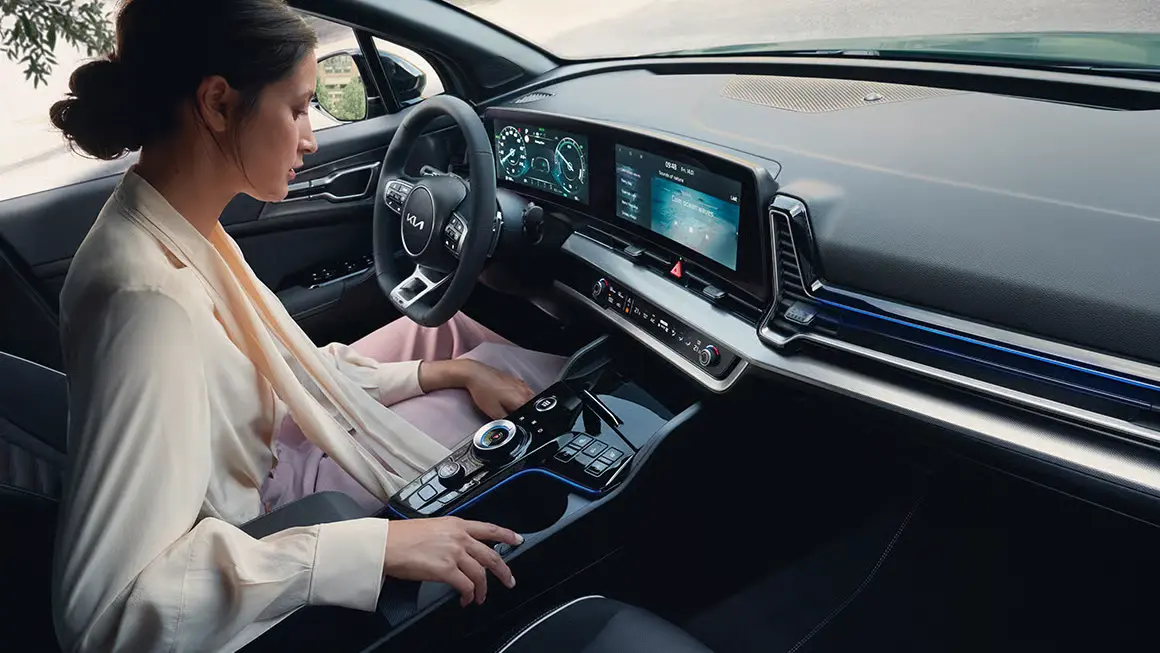 Frau sitzt im Innenraum eines Kia Sportage HEV GTL und bedient die Mittelkonsole.