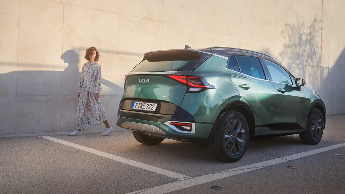 Kia Sportage HEV GTL MY22 in Grün auf einer Straße neben einer Frau.
