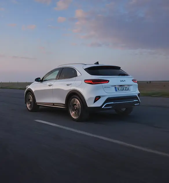 Ein weißer Kia XCeed fährt auf einer Landstraße bei Sonnenuntergang.