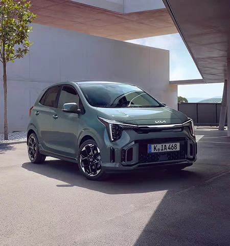 Ein grüner Kia Picanto steht auf einem Parkplatz vor einem modernen Gebäude.