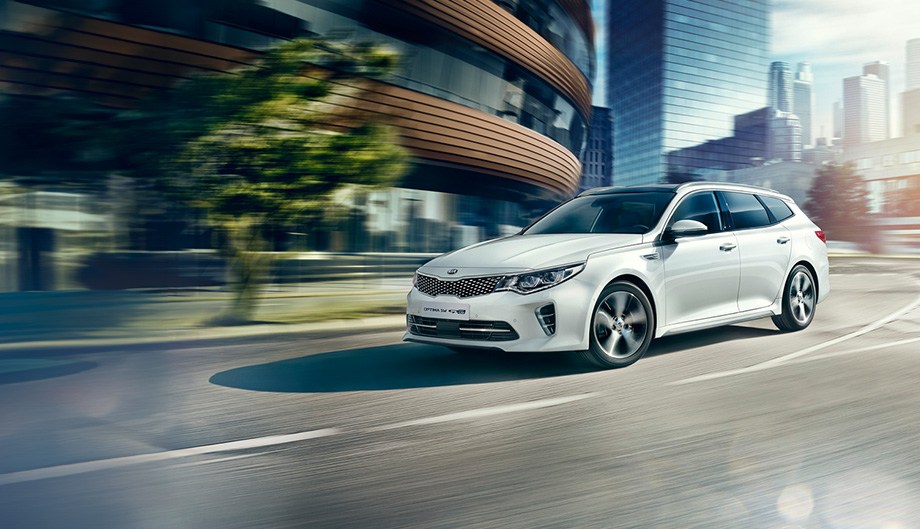 Ein weißer Kia Optima fährt auf einer städtischen Straße.