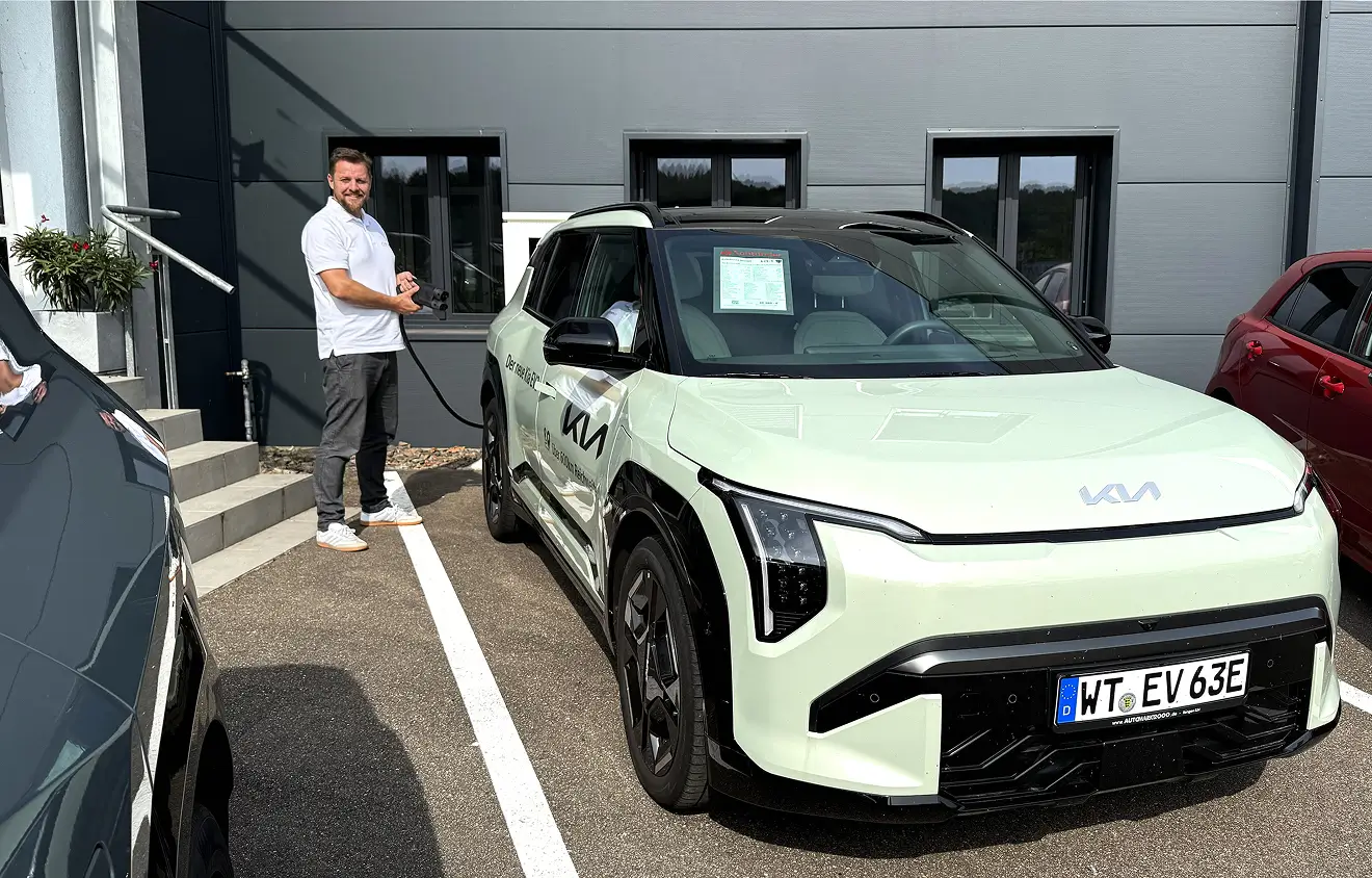 e-ladestation-automarkt2000 Ein Mann lädt ein weißes KIA-Elektroauto an einer Ladestation auf.
