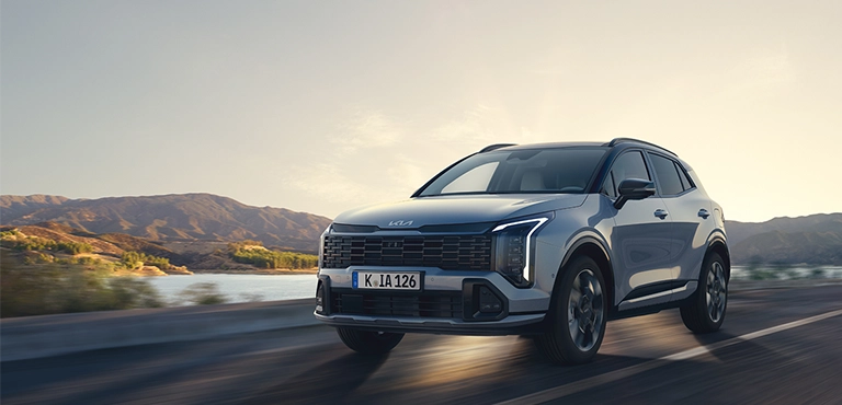 Kia-SUV fährt auf offener Landstraße vor Berglandschaft bei Sonnenuntergang.