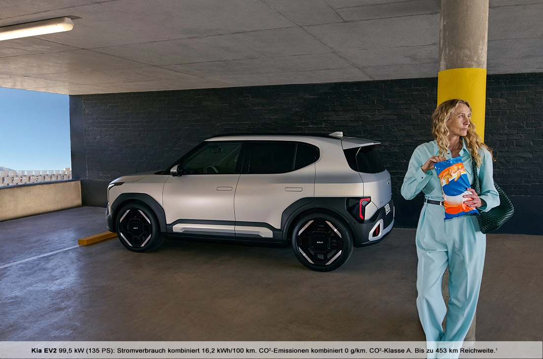 Kia EV2 in Parkgarage; Frau mit Chips-Tüte steht daneben.